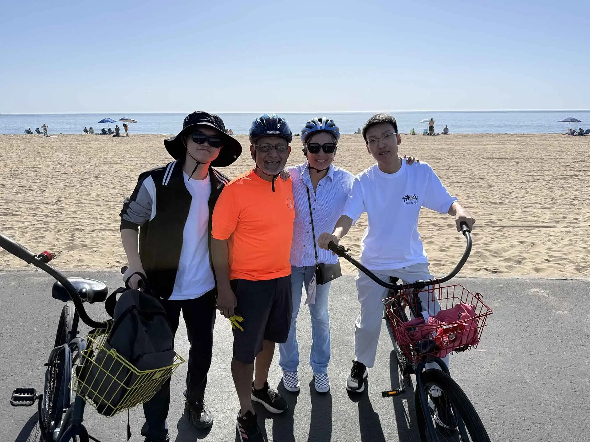 International participants and host family members pose with bicycles on a sunny beach, sharing a cross-cultural homestay experience in the United States.