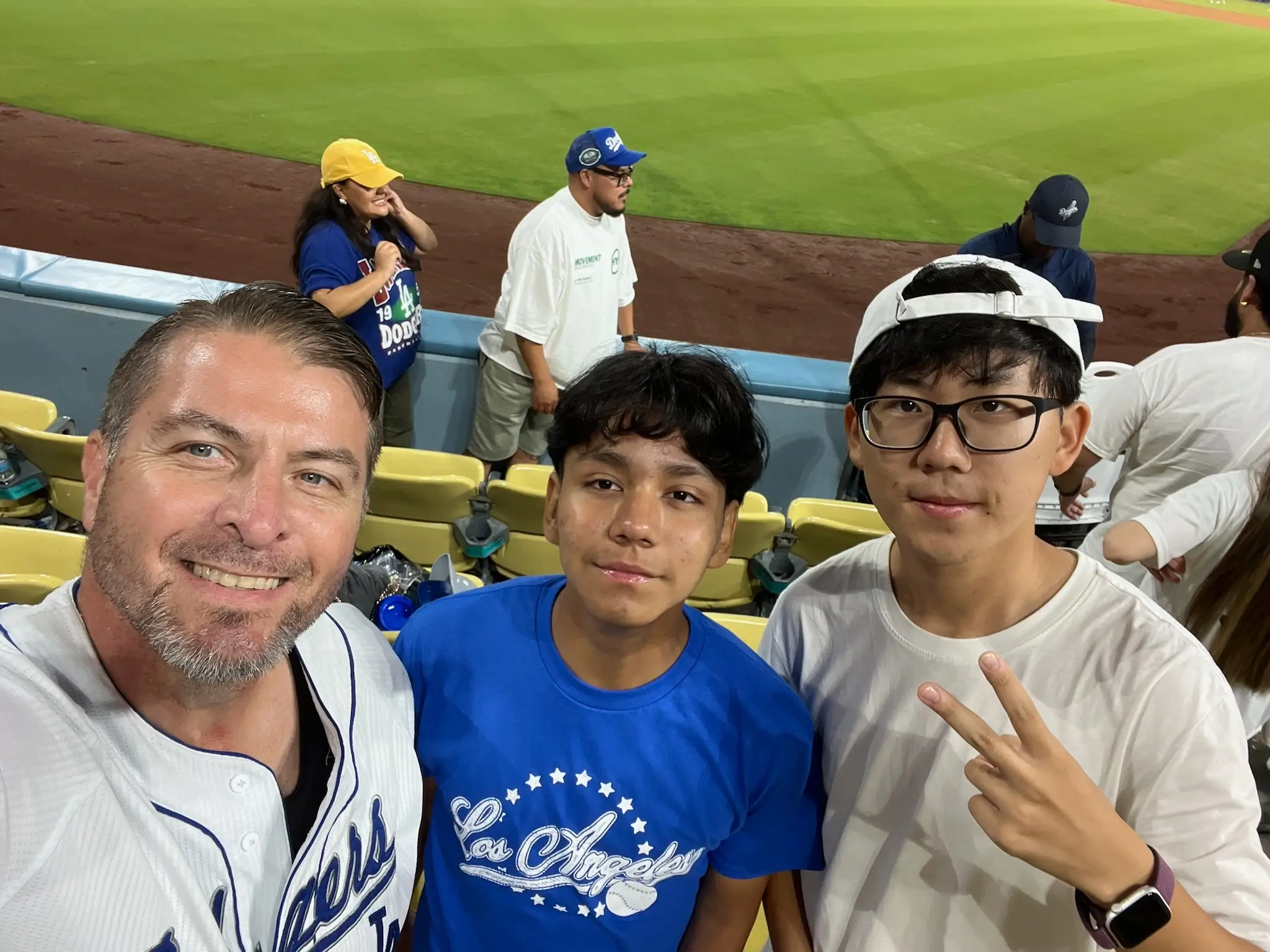 American host family member and international participants pose together at a baseball game during a U.S. homestay cultural exchange program.